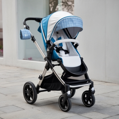 A stylish blue and white baby stroller with a coordinating plaid sunshade and matching side storage pouch, parked on a paved walkway near a modern white building. The stroller features a sturdy frame, cushioned seat, and adjustable handlebar for added convenience.