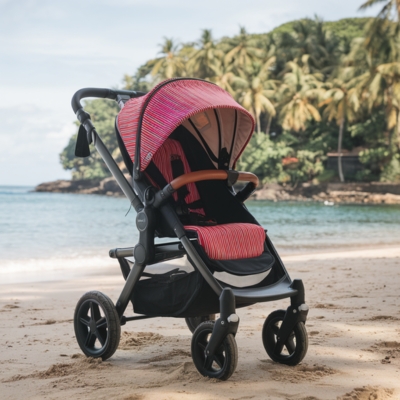 A red and black striped single stroller parked on a tropical beach with golden sand, crystal-clear water, and lush palm trees in the background. Ideal for parents who love seaside strolls and outdoor adventures.