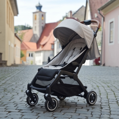 Compact and lightweight travel stroller with a beige canopy, designed for cobblestone streets and urban travel, set in a charming European town setting.