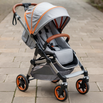 Modern travel stroller with a gray canopy, orange accents, and leather-accented handles, designed for easy maneuverability on paved pathways.